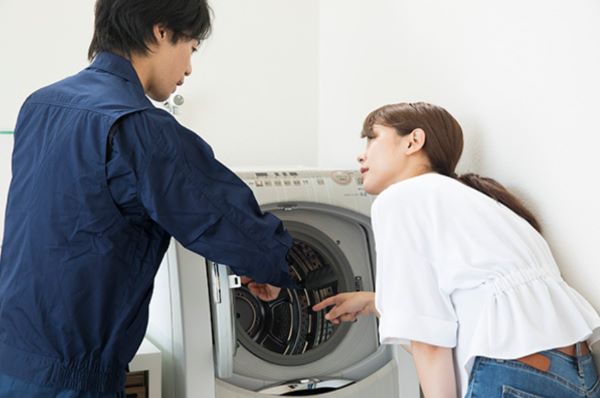 洗濯機を前に、説明する男性と、説明を聞く女性